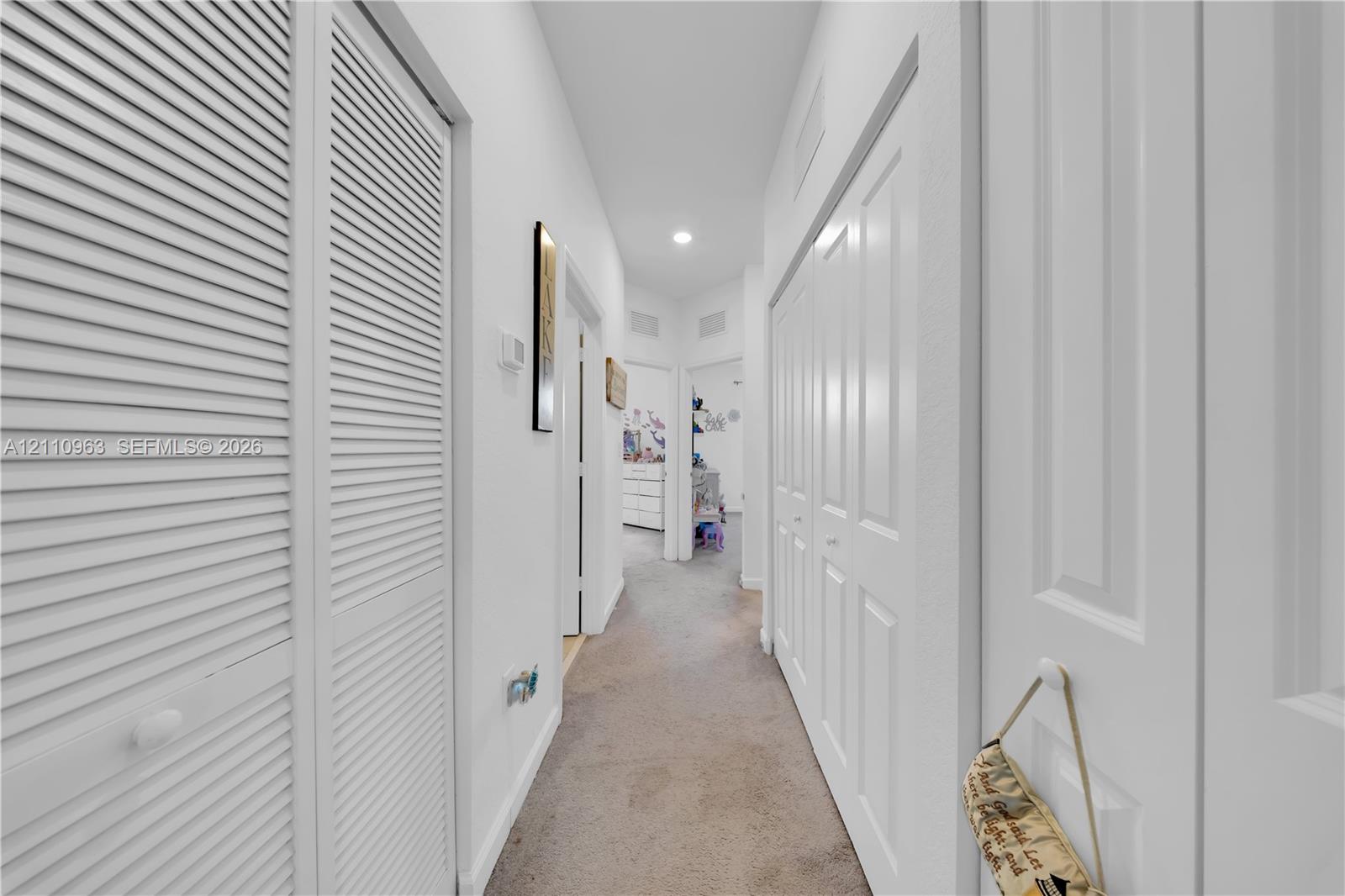 Hallway featuring dual sets of white louvered-style closet doors, recessed lighting, and neutral carpeting