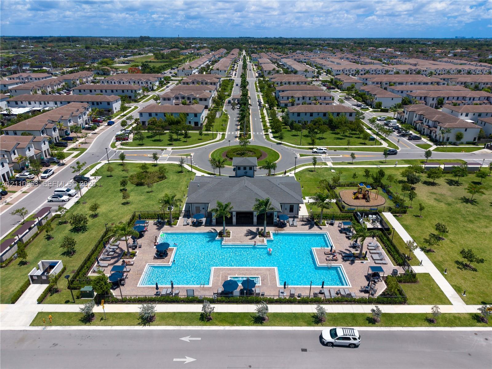 Community recreation center featuring an expansive swimming pool, paver deck, clubhouse building, and playground area