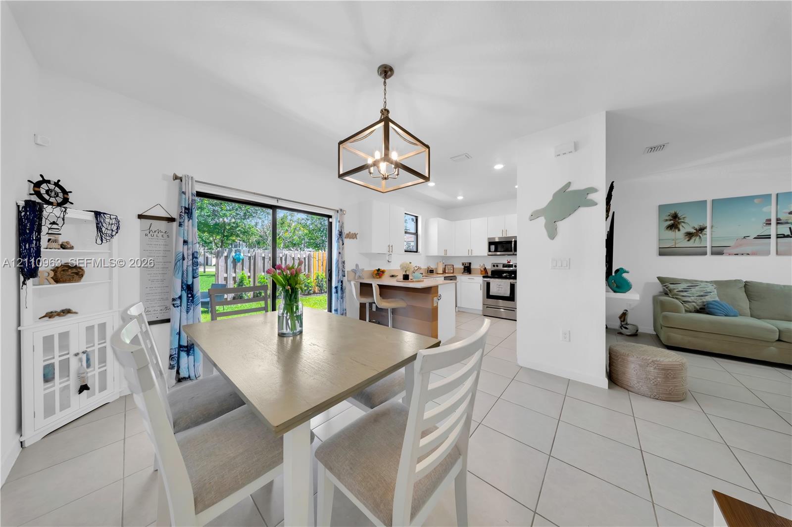 Open-concept interior featuring light-toned tile flooring, geometric pendant lighting, built-in white cabinetry, quartz-surface kitchen island, and sliding glass doors
