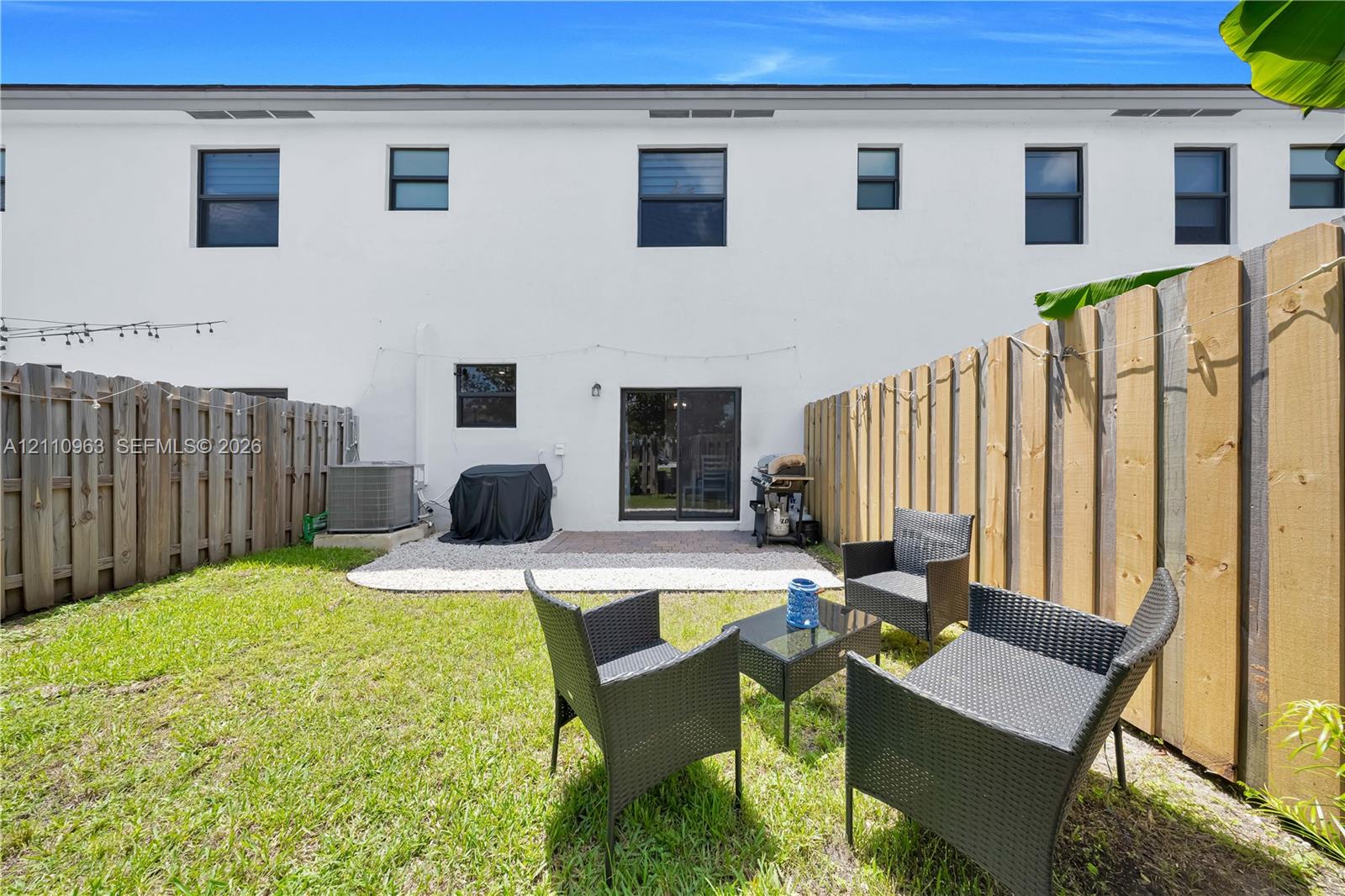Rear exterior featuring a smooth-stucco facade, a paved concrete patio, and a fully fenced yard with a manicured lawn