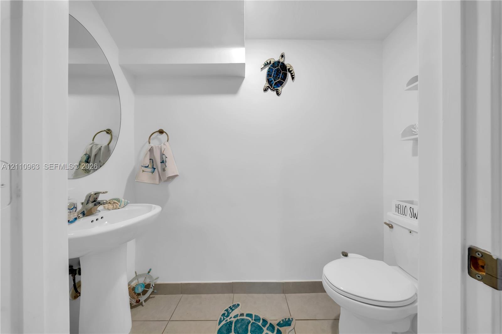 Powder room featuring a pedestal sink, arched wall mirror, ceramic tile flooring, and integrated shelving