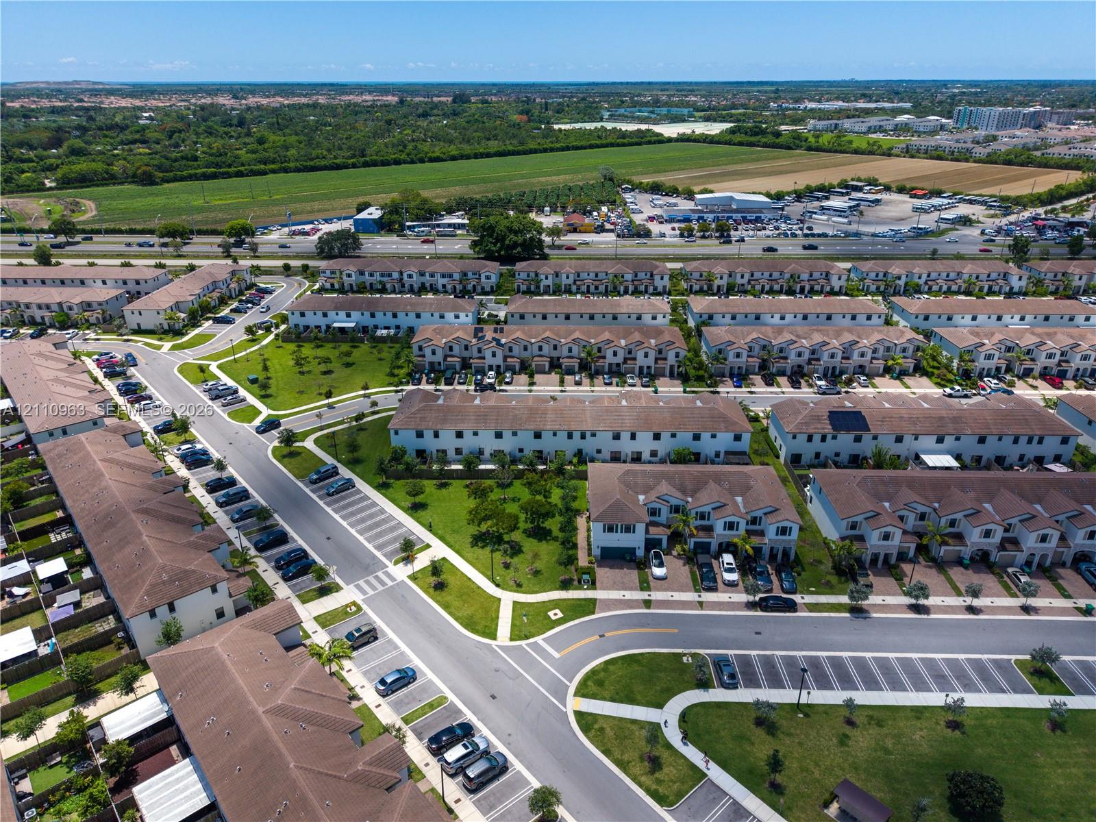 Aerial perspective of a multi-unit residential community featuring paved streets, designated surface parking, manicured common green space, and shingle-roof architecture