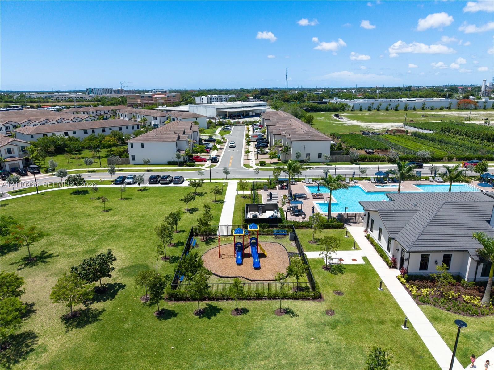 Community grounds featuring a swimming pool, fenced playground, manicured lawn, and paved walking paths