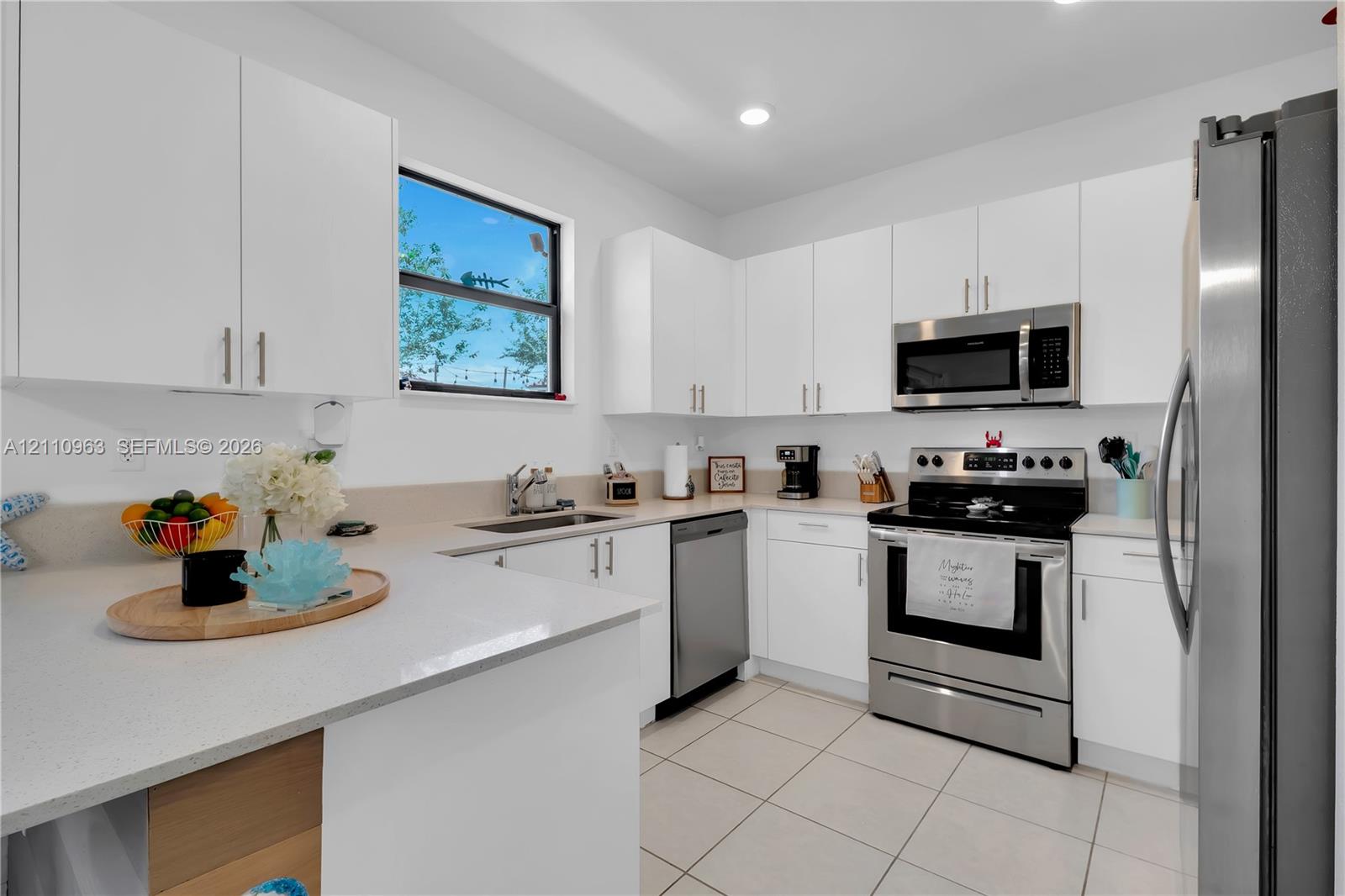 Kitchen featuring white cabinetry, solid-surface countertops, tile flooring, stainless steel appliances, and a double-basin undermount sink