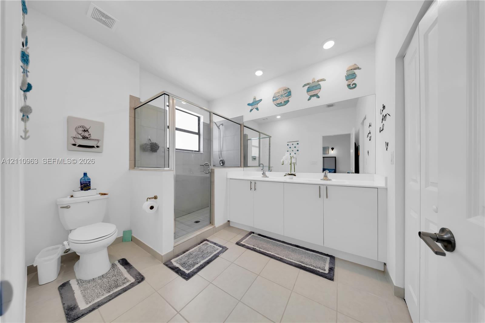 Bathroom featuring a double-sink vanity with white cabinetry and a full-width wall mirror, walk-in shower with a glass enclosure, and neutral tile flooring