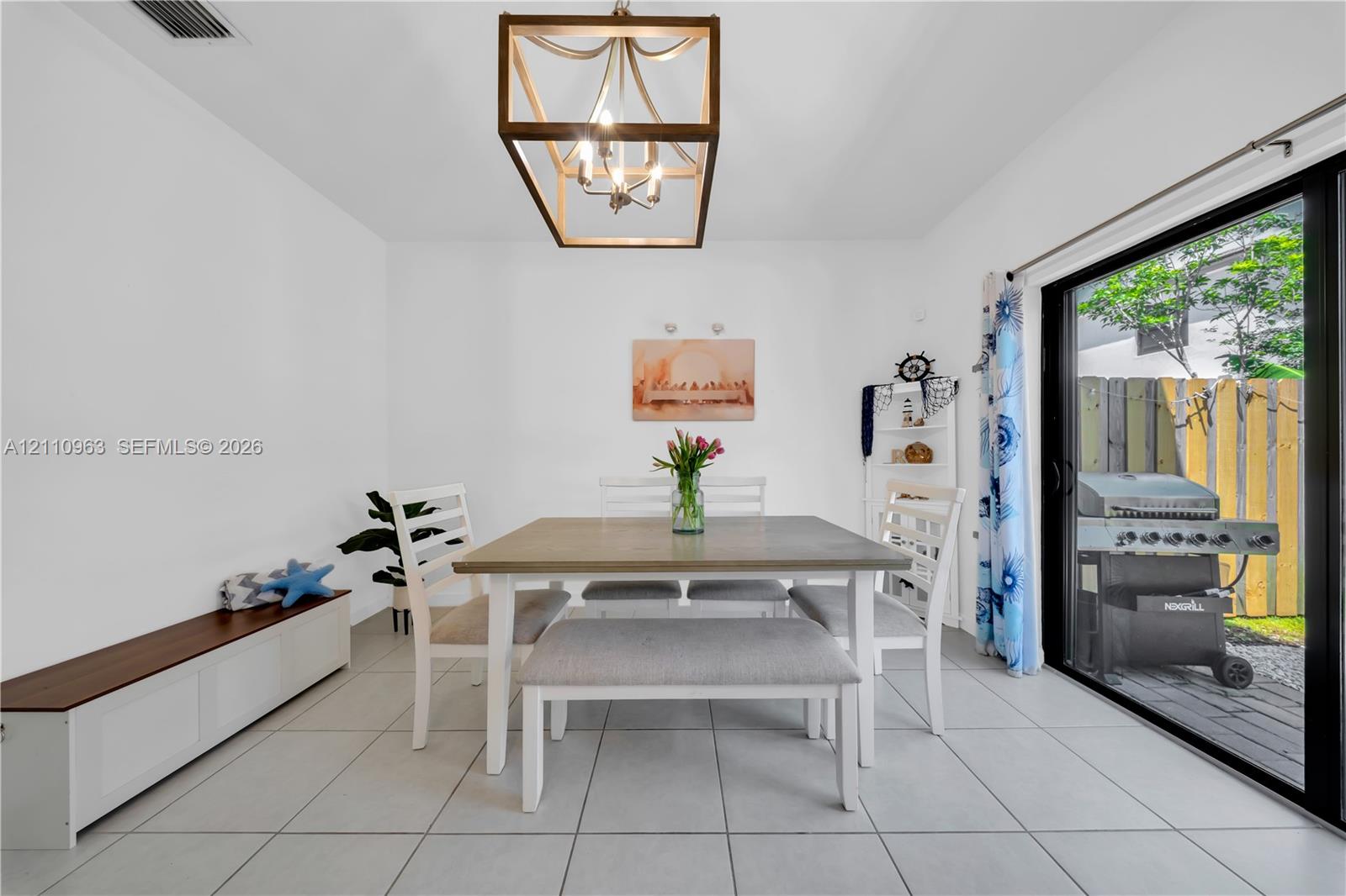 Dining area featuring large-format ceramic tile flooring, a geometric metallic lantern-style pendant light, and a sliding glass door providing external access