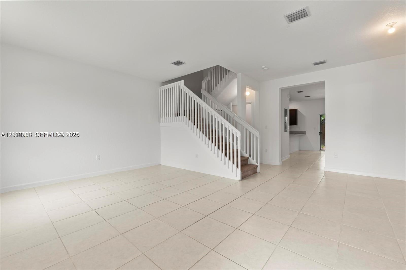Open interior space featuring neutral tile flooring, staircase with white railing, and flush-mount ceiling lighting