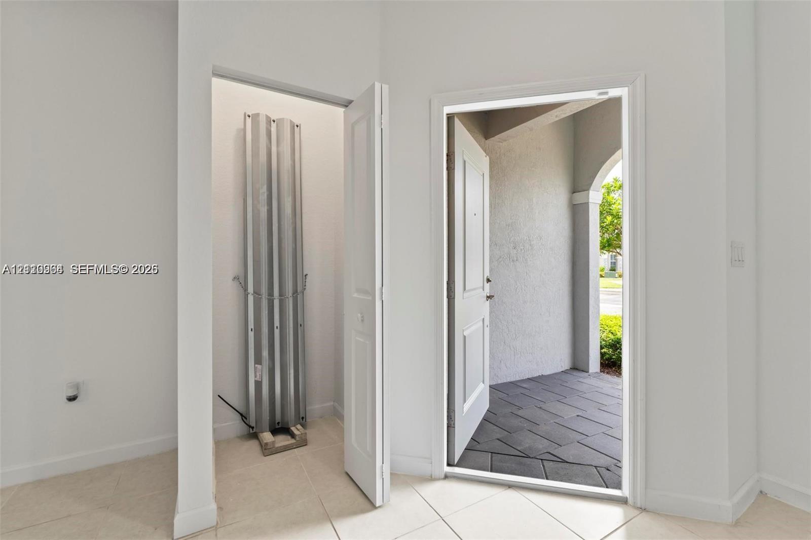 Entryway featuring large-format tile flooring, a storage closet, a white paneled door, and a tiled exterior porch with an arched architectural detail