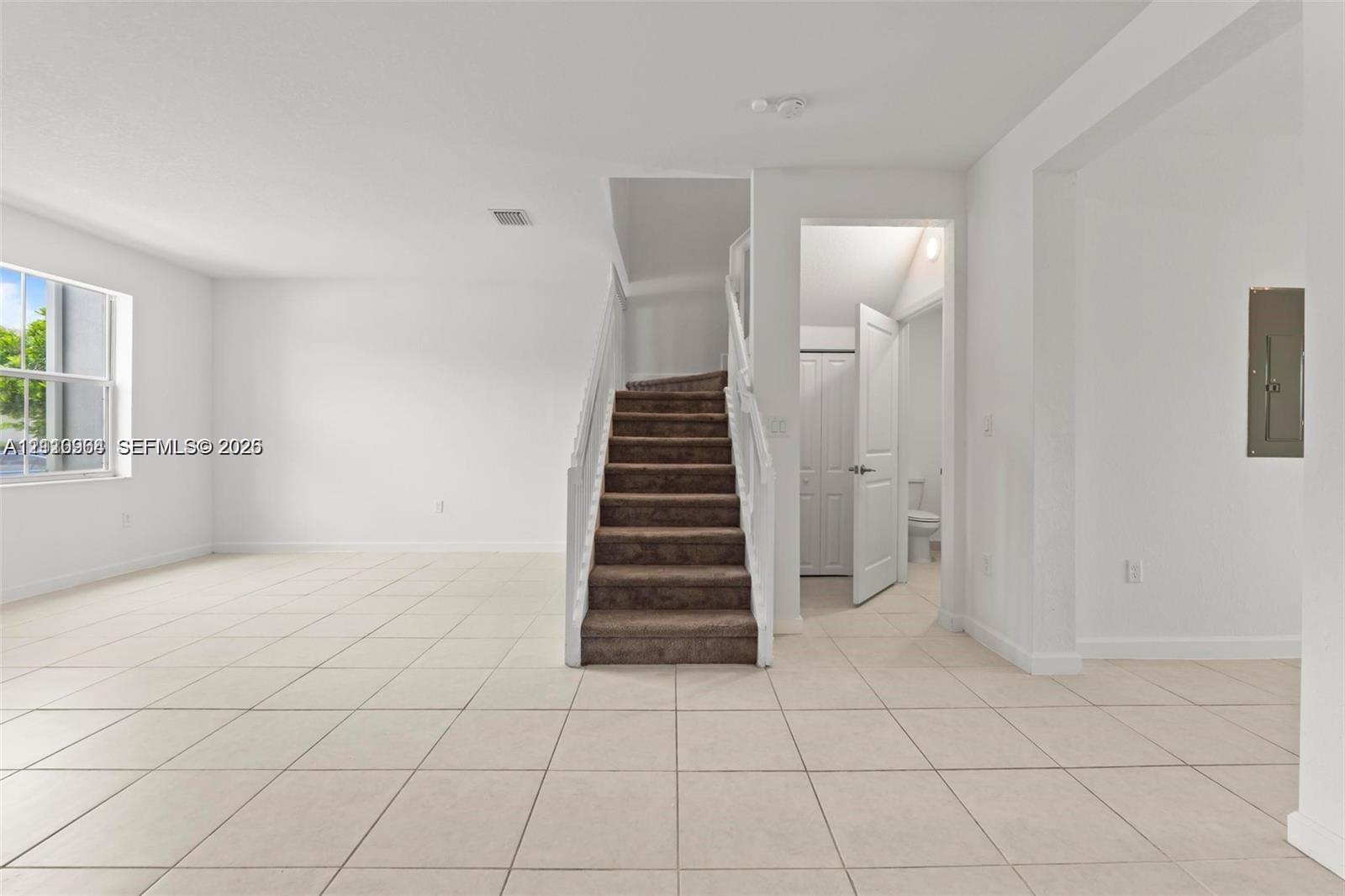 Open-concept floor plan featuring large-format ceramic tile flooring, a staircase with white painted balusters, and a single-hung window with natural light