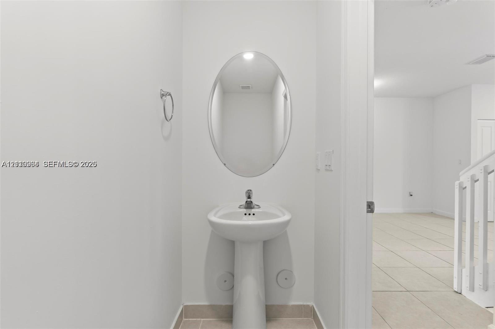 White porcelain pedestal sink with a chrome single-handle faucet, oval wall-mounted mirror, and wall-mounted metal towel ring