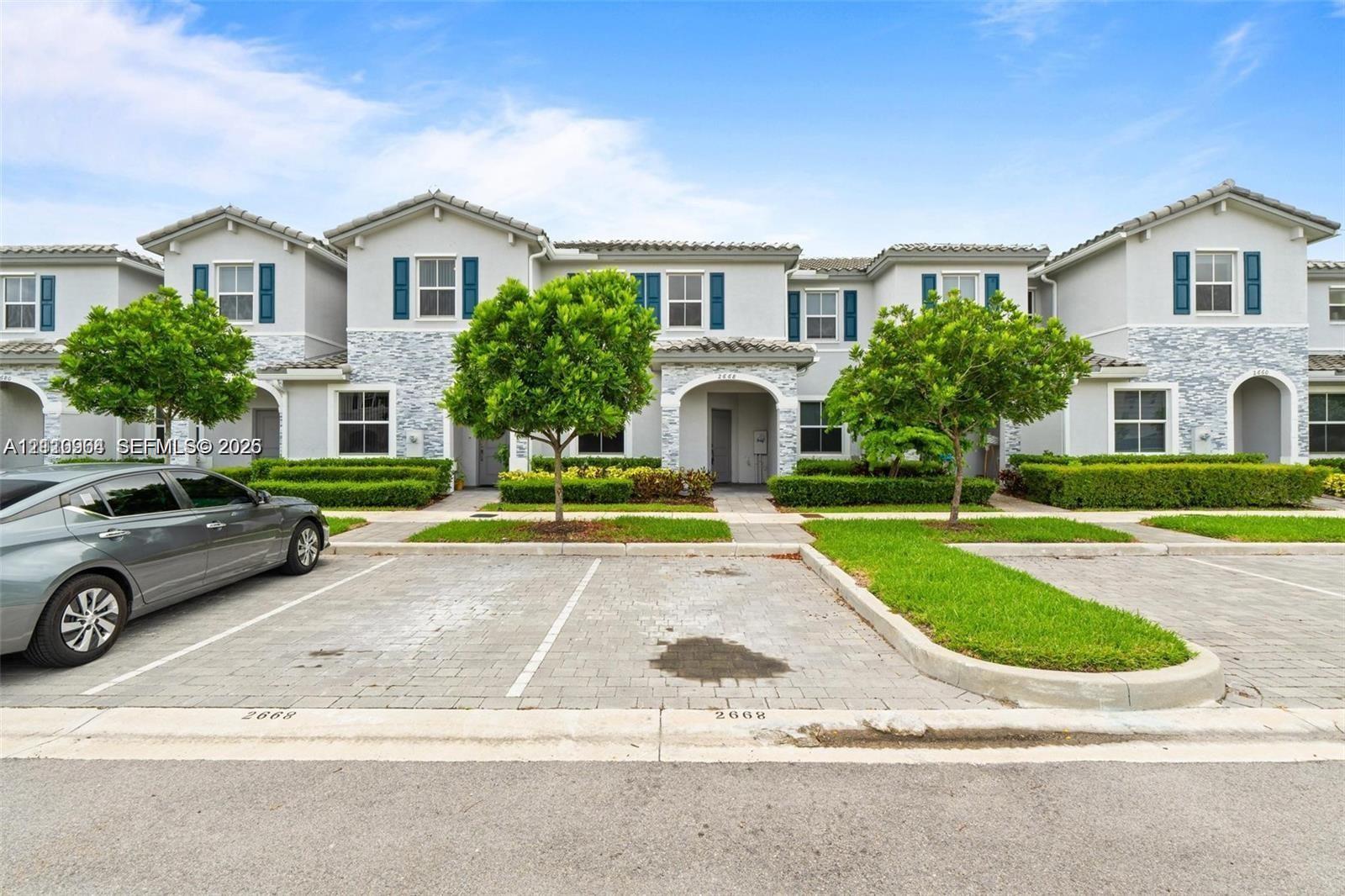Multi-unit exterior featuring light gray stucco siding with stone veneer accents, arched entryways, and dedicated paver parking spaces