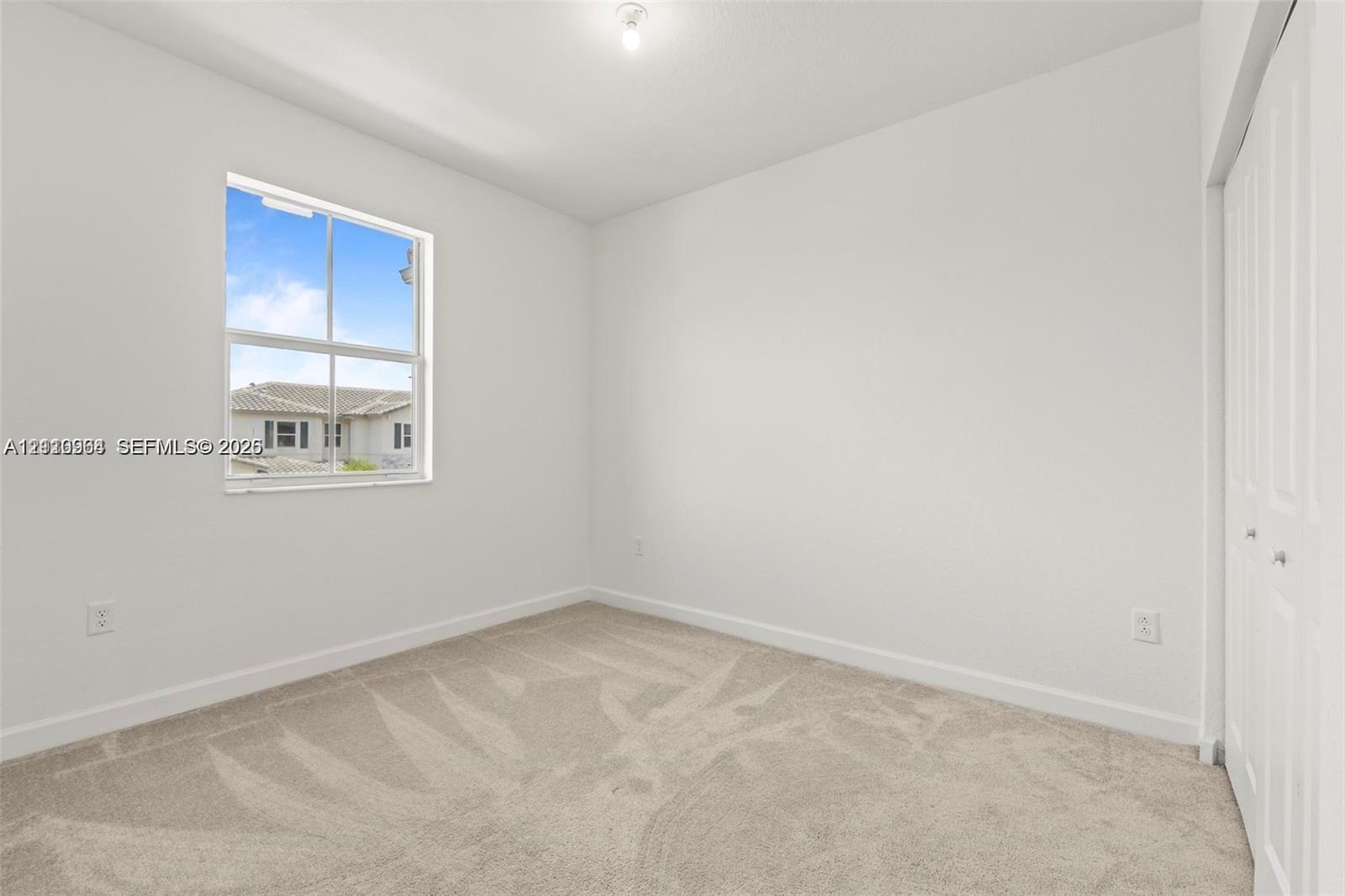 Neutral interior featuring wall-to-wall carpeting, a single-hung window with exterior muntins, and a multi-panel bifold closet door