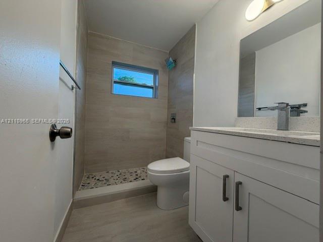 Bathroom featuring a white shaker-style vanity with a solid surface countertop, tiled shower enclosure with river stone flooring, and integrated wall-mounted lighting