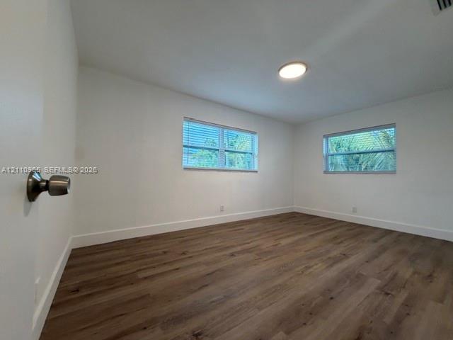 Interior room featuring wood-finish flooring, two windows with horizontal blinds, and a flush-mount ceiling light fixture