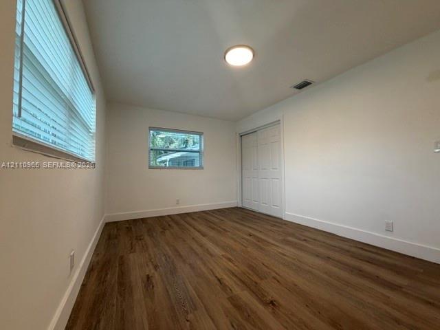Interior space featuring wood-finish flooring, white walls, double-door sliding closet, and windows with horizontal blinds