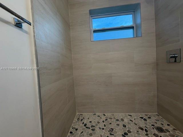 Walk-in shower enclosure featuring large-format neutral-tone tile walls, river stone flooring, an integrated rectangular window, and polished chrome fixtures