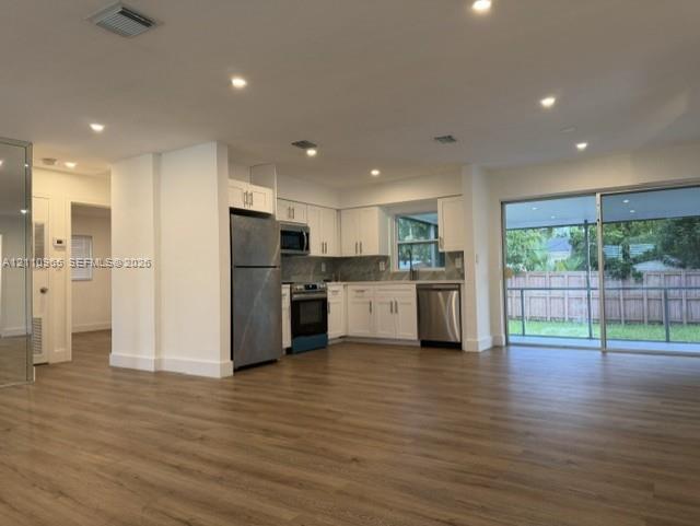 Kitchen featuring white shaker-style cabinetry, stainless steel appliances, and wood-finish flooring, accompanied by recessed lighting and a sliding glass door Kitchen featuring white shaker-style cabinetry, stainless steel appliances, and wood-finish flooring, accompanied by recessed lighting and a sliding glass door