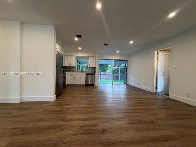 Open-concept interior featuring wood-finish flooring, recessed lighting, white cabinetry, stainless steel appliances, and sliding glass doors