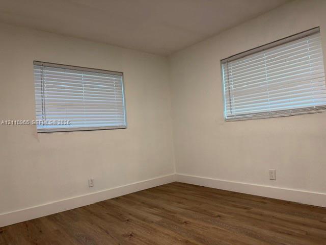 Neutral interior featuring wood-finish flooring, white walls, and two windows equipped with horizontal blinds