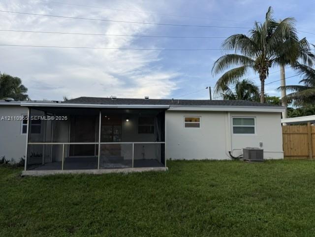 Rear exterior featuring a screened-in lanai, concrete patio, expansive lawn, wood fencing, and mature palm trees Rear exterior featuring a screened-in lanai, concrete patio, expansive lawn, wood fencing, and mature palm trees