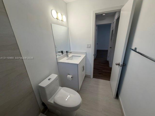 Bathroom featuring a single-sink vanity with a solid-surface countertop, three-light wall-mounted fixture, rectangular mirror, and light-toned tile flooring
