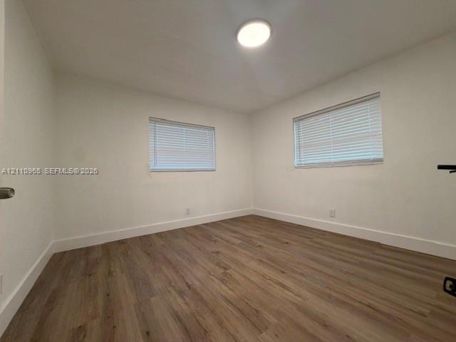 Room featuring wood-finish flooring, two windows with horizontal blinds, and a flush-mount ceiling light fixture