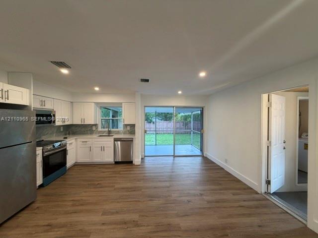 Kitchen featuring white shaker-style cabinetry, stone-patterned backsplash, stainless steel appliances, and wood-finish flooring, accompanied by sliding glass doors opening to a screened porch