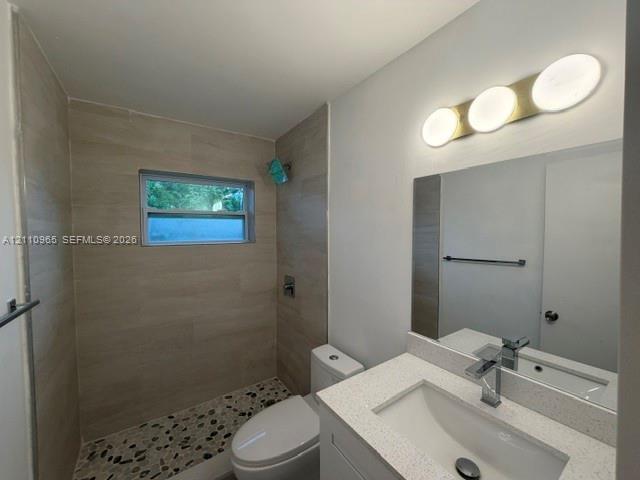 Bathroom featuring a walk-in shower with stone-style pebble flooring and large-format wall tile, a white quartz vanity countertop, and a contemporary three-light fixture