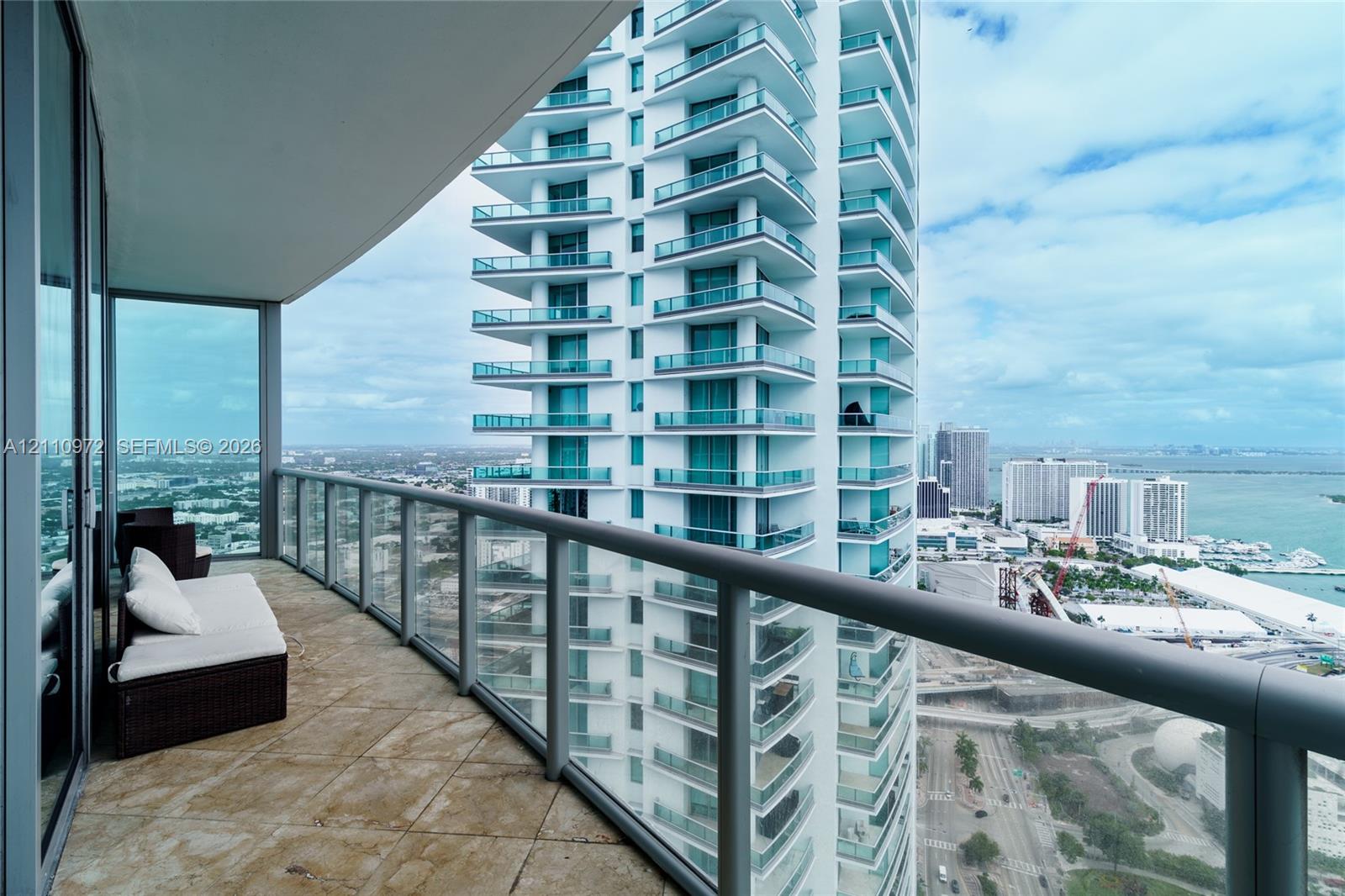 Covered outdoor balcony featuring stone tile flooring and glass railings Covered outdoor balcony featuring stone tile flooring and glass railings