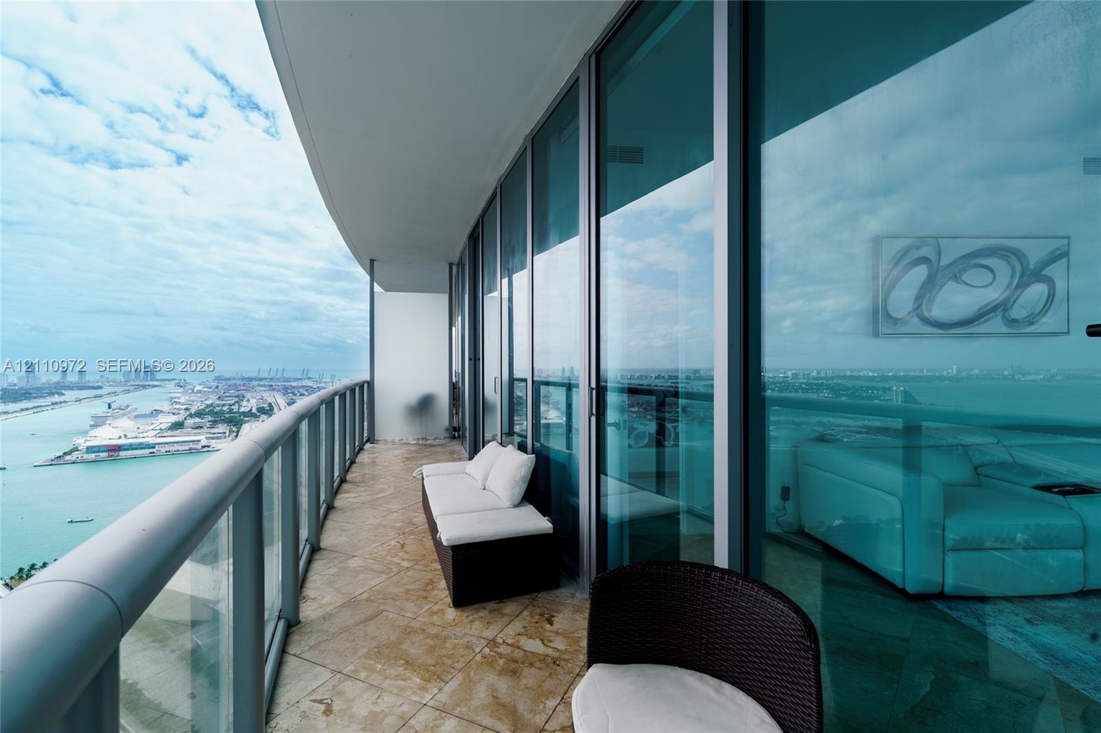 Curved balcony featuring floor-to-ceiling glass paneling, stone tile flooring, and a metal railing Curved balcony featuring floor-to-ceiling glass paneling, stone tile flooring, and a metal railing