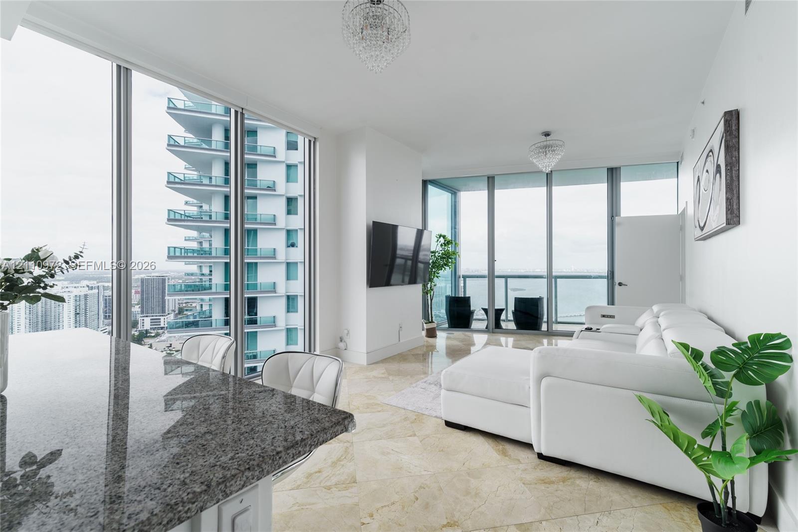 Floor-to-ceiling windows, natural stone flooring, dual crystal chandeliers, and expansive glass balcony enclosure