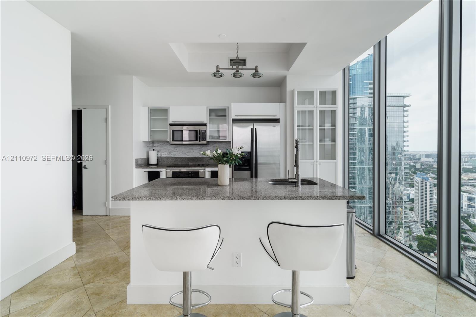 Kitchen featuring stone-topped island, stainless steel appliances, floor-to-ceiling windows, and tile flooring