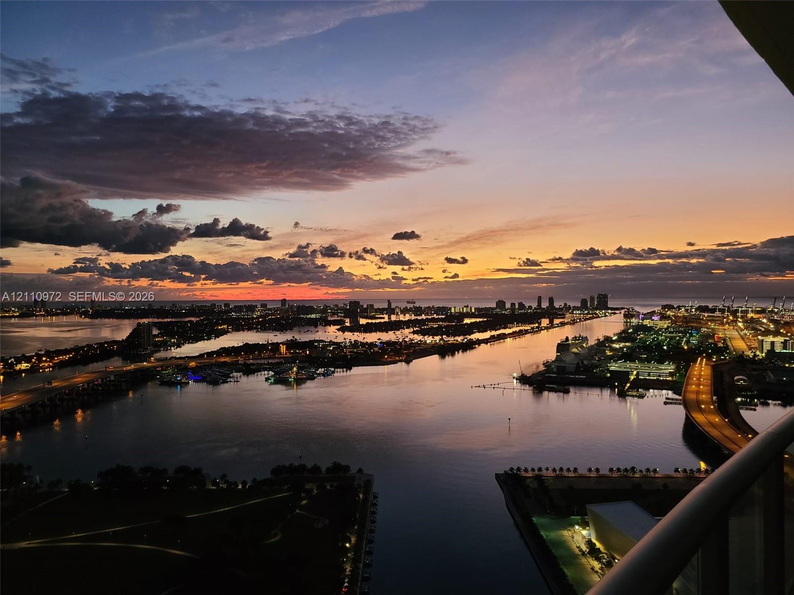 Elevated balcony featuring a panoramic cityscape, waterfront scenery, and horizon sunset Elevated balcony featuring a panoramic cityscape, waterfront scenery, and horizon sunset