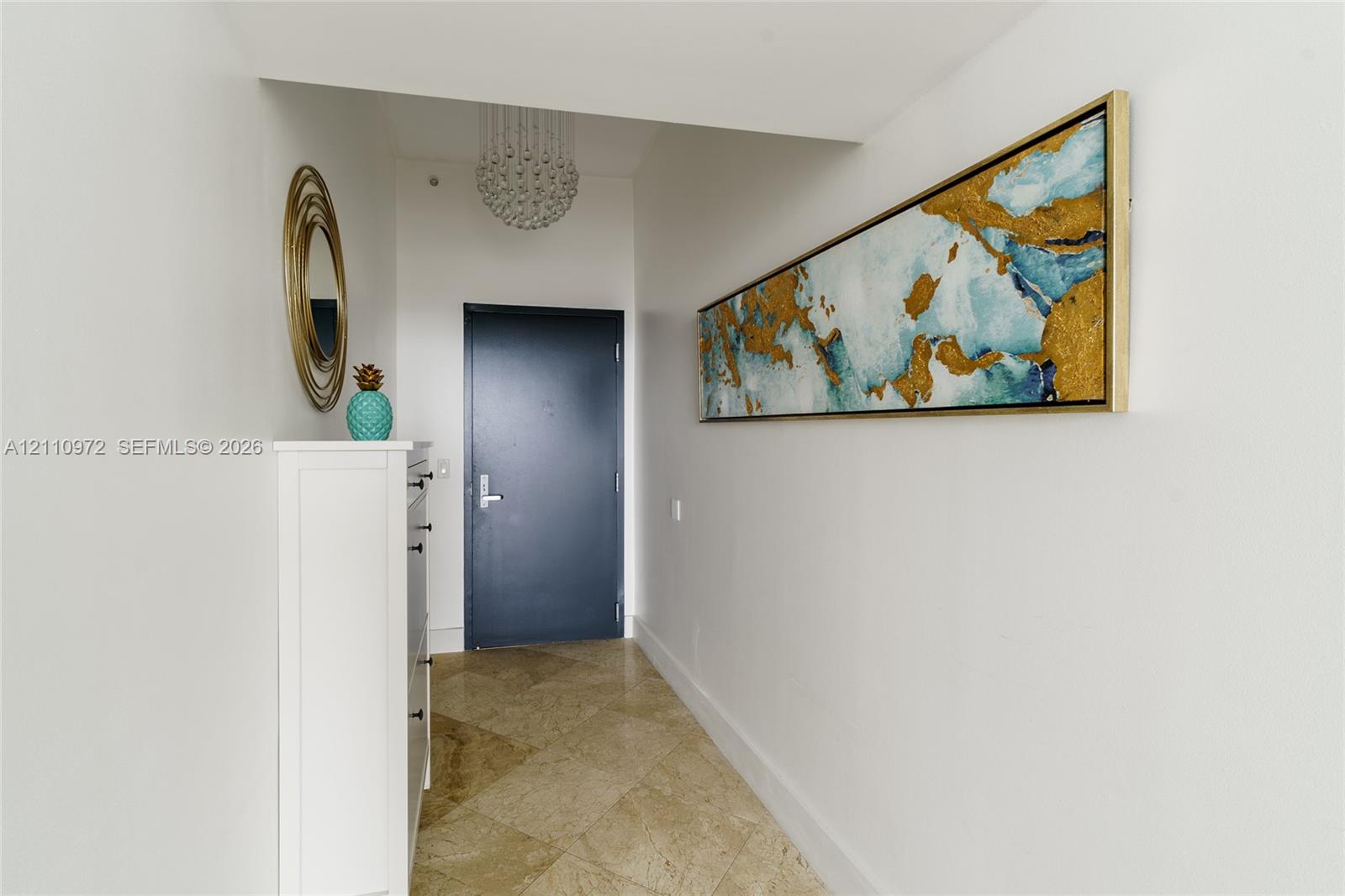 Entryway featuring diagonal-set stone tile flooring, a tiered crystal drum chandelier, and a solid-core door with brushed metal hardware