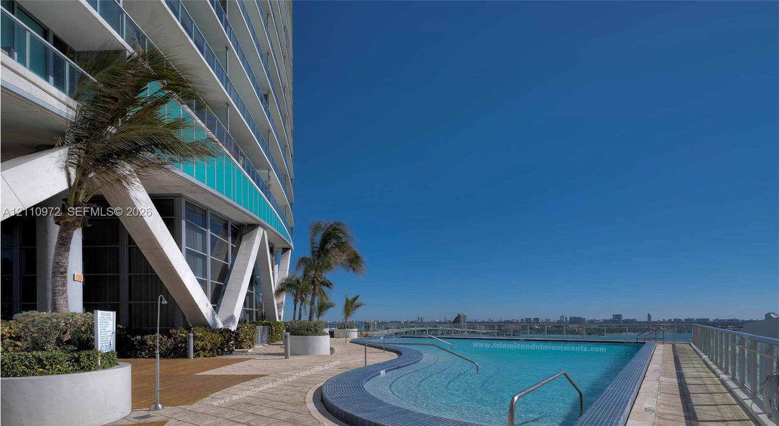 Outdoor pool featuring a curved tiled edge, tile decking, integrated tiered steps, and metal railings, set against an architectural facade with structural support beams and glass balcony partitions
