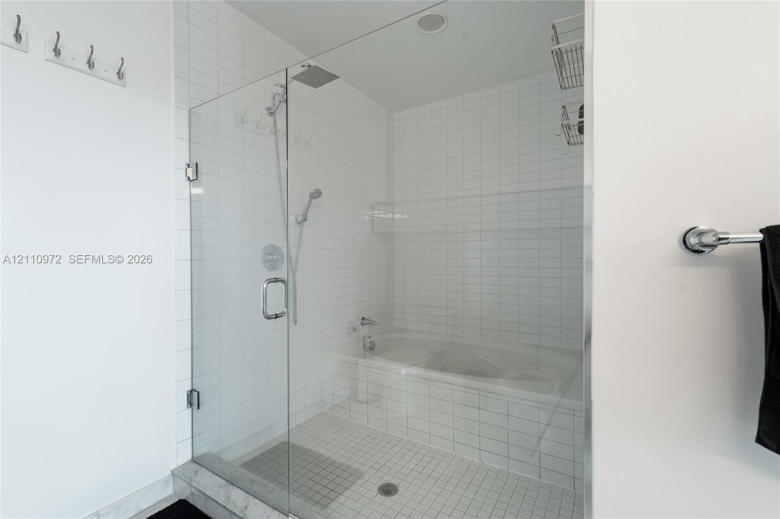 Walk-in shower with frameless glass door, soaking tub, square white wall tiling, rain-style shower head, and chrome fixtures