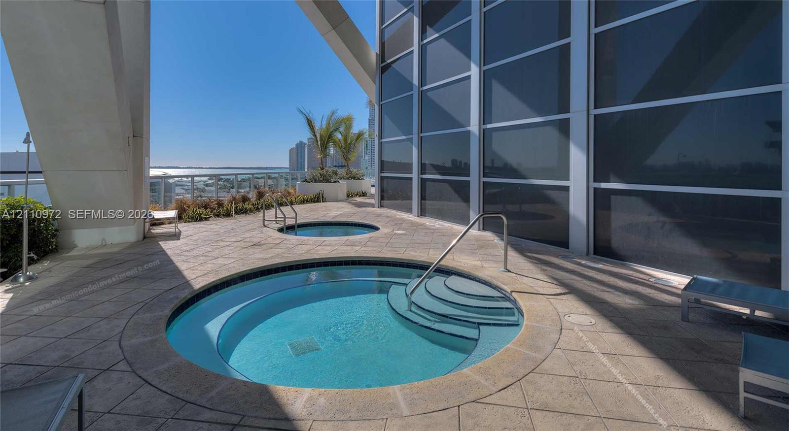 Terrace featuring two circular in-ground spas, stone-paver flooring, metal handrails, and floor-to-ceiling glass paneling