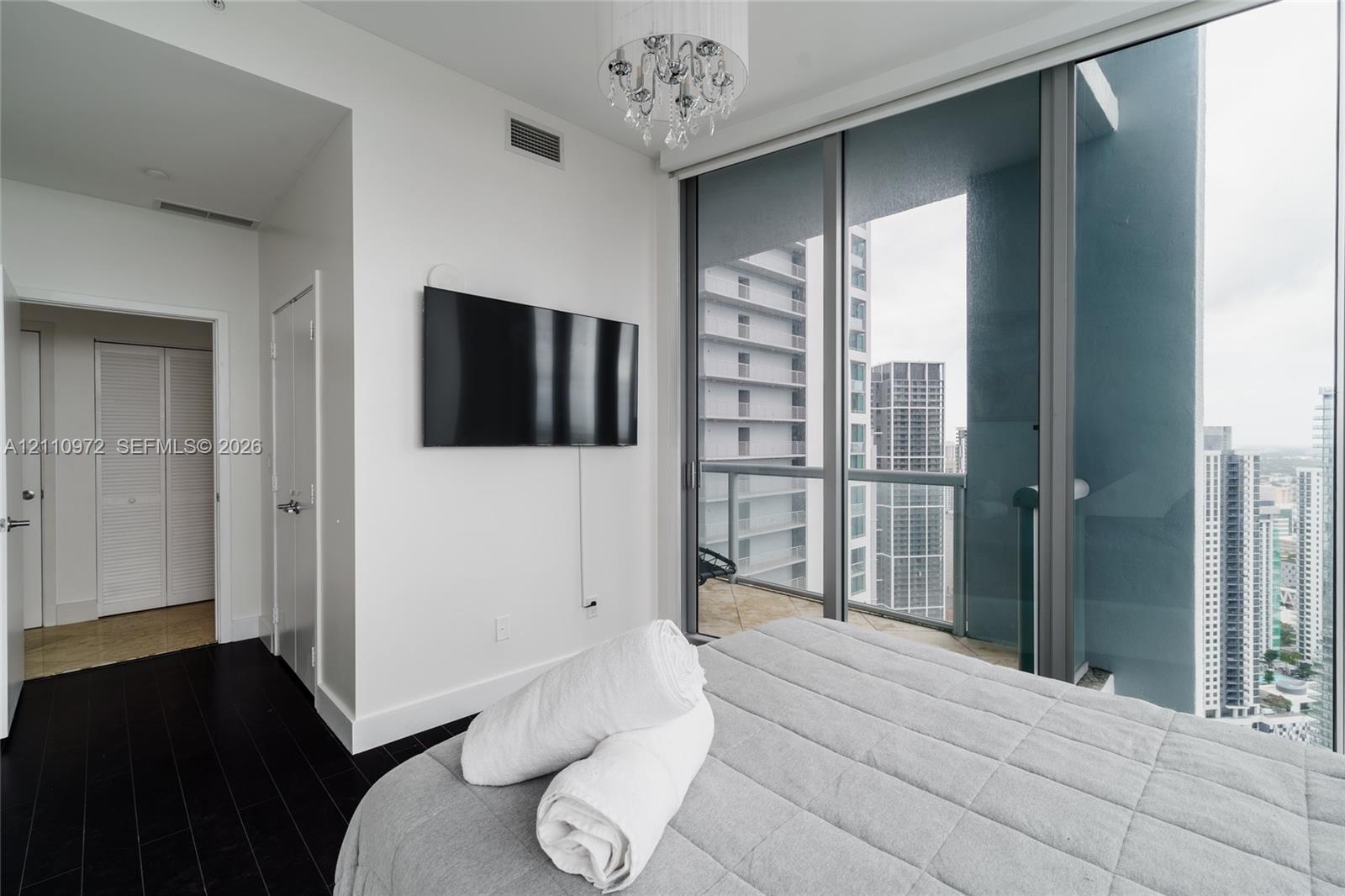 Floor-to-ceiling windows, dark wood-finish flooring, glass-railing balcony, and a decorative chandelier