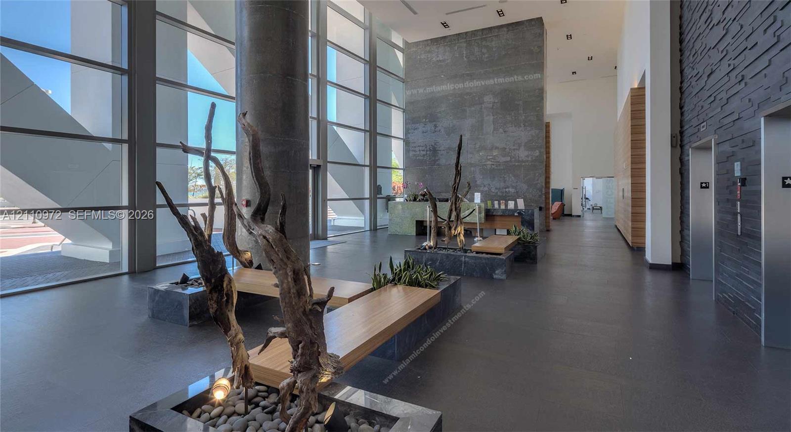 Floor-to-ceiling windows, soaring double-height ceilings, stone-finish feature wall, matte-finish tile flooring, and metallic elevator bank