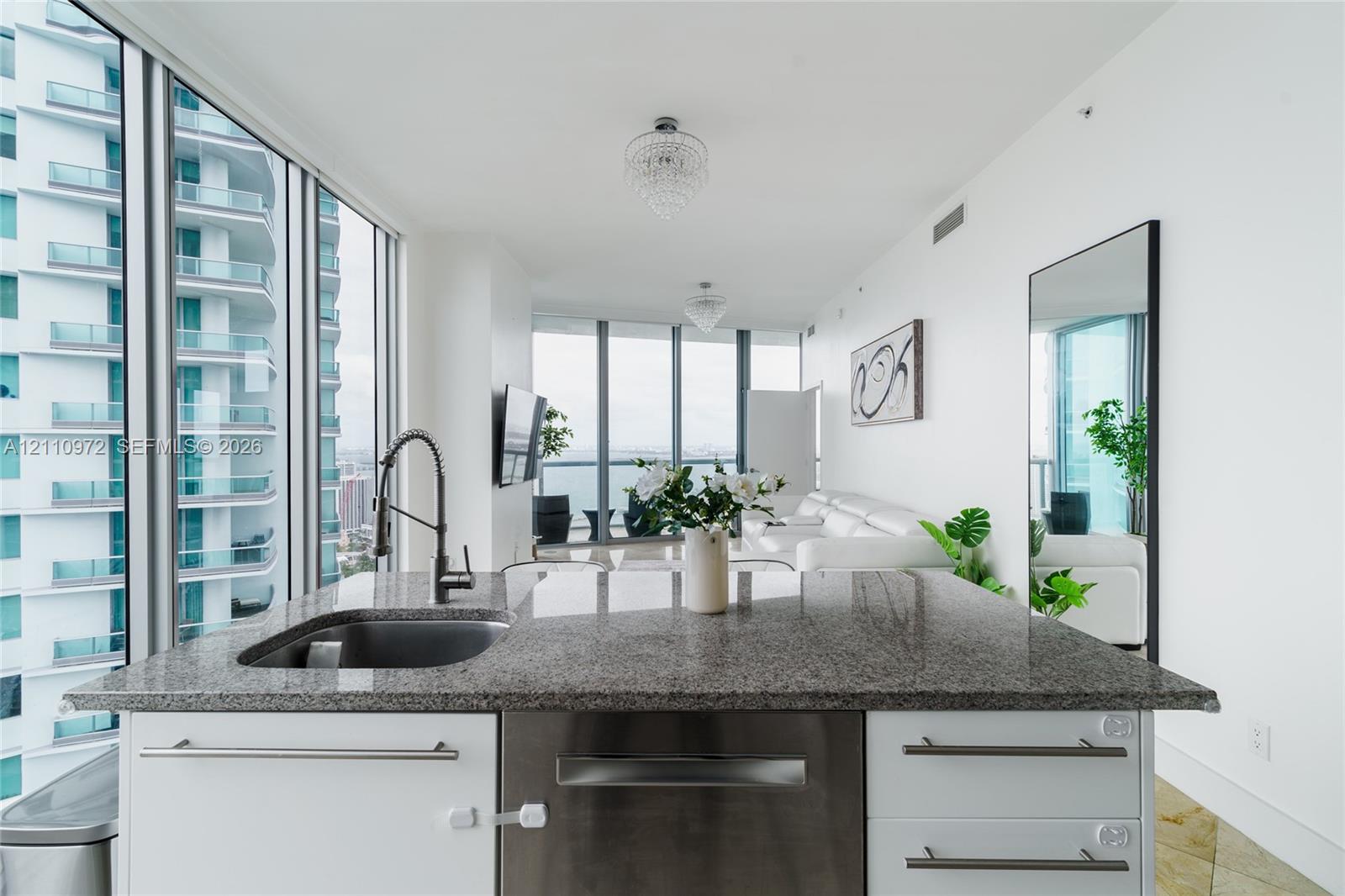 Kitchen island featuring stone countertops, an undermount sink, stainless steel dishwasher, and white cabinetry with metal hardware Kitchen island featuring stone countertops, an undermount sink, stainless steel dishwasher, and white cabinetry with metal hardware