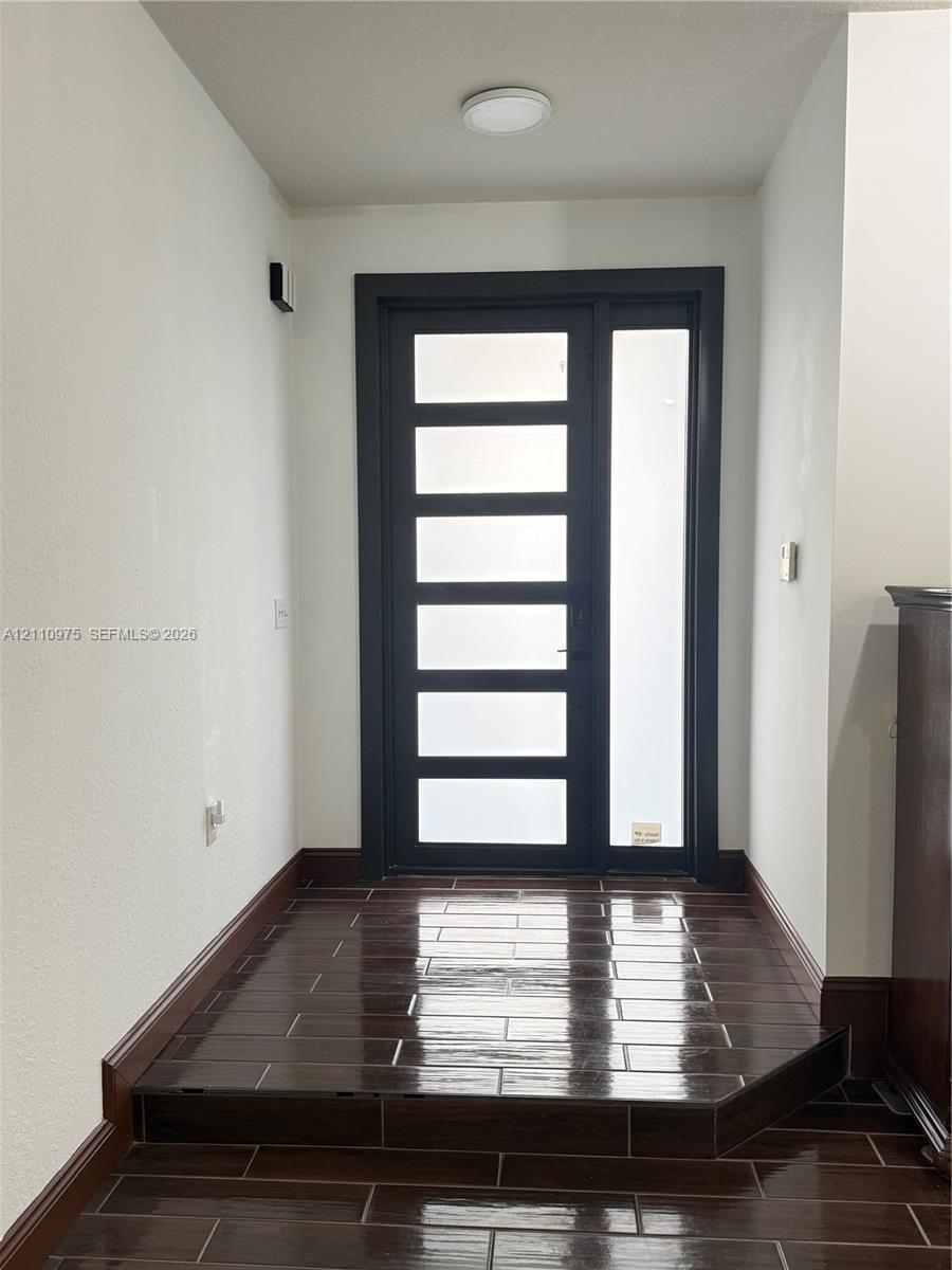 Modern entry featuring a dark-framed door with multi-panel glass inserts, a matching full-length glass sidelight, and dark-toned rectangular tile flooring