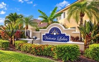 Stucco monument signage featuring decorative tile inlay and manicured tropical landscaping with mature palm trees