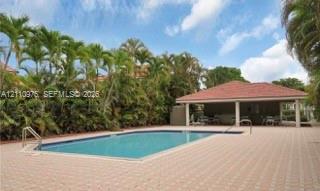 In-ground pool with metal handrails surrounded by a spacious paver deck and a covered pavilion featuring a hipped tile roof