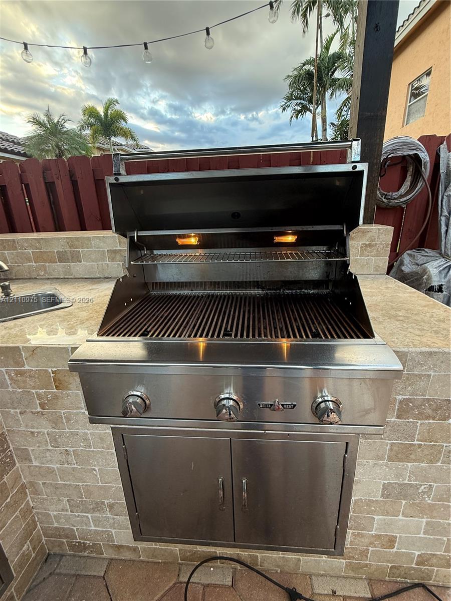 Outdoor kitchen featuring a built-in stainless steel grill, natural stone masonry surround, integrated stainless steel storage cabinet, and an inset sink