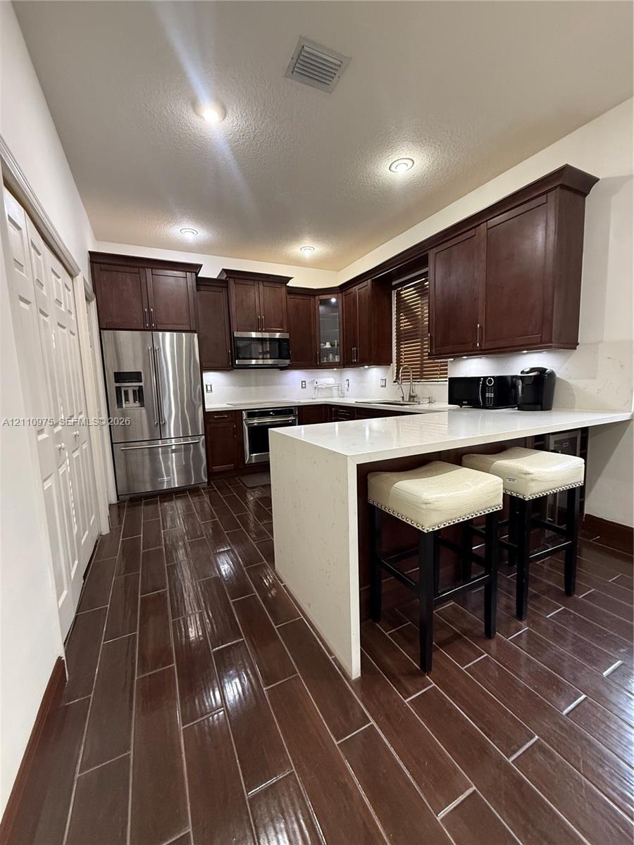 Kitchen featuring stained wood cabinetry, quartz countertops with a waterfall edge, stainless steel appliances, and dark wood-finish tile flooring