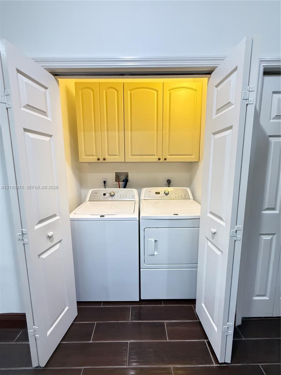 Laundry closet featuring white bi-fold doors, upper cabinet storage with raised-panel doors, and tile flooring