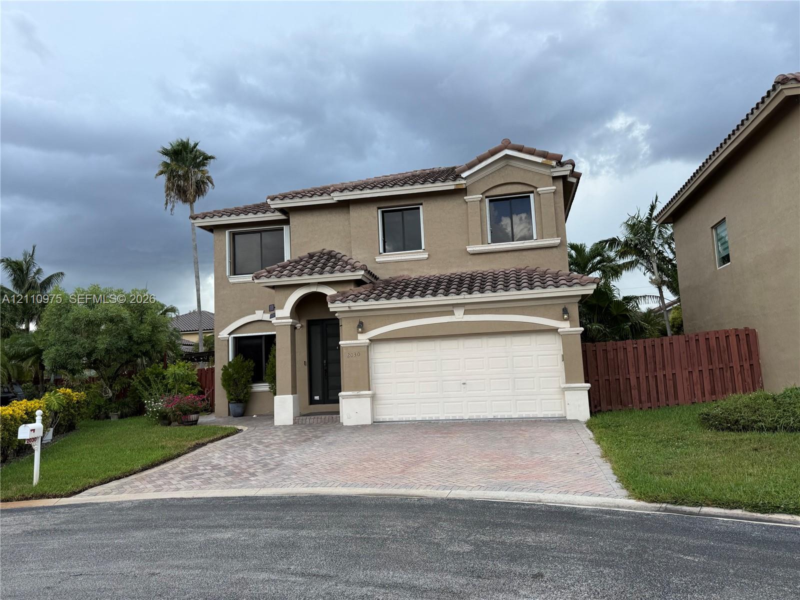 Two-story residence featuring a terracotta-tiled roof, stucco exterior, decorative archway at the main entrance, and a paved stone driveway leading to an attached two-car garage