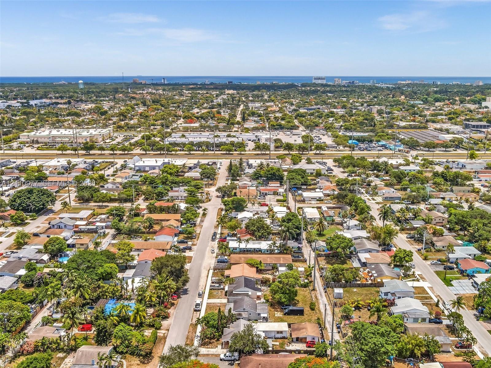 Aerial perspective featuring an established residential neighborhood with mature canopy trees and proximity to the coastline