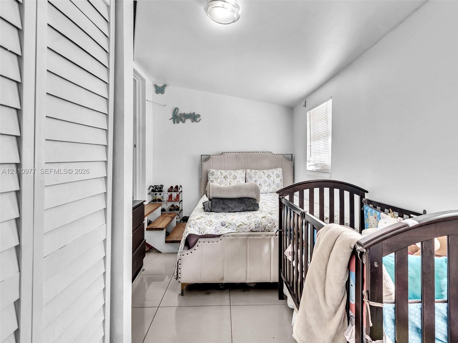Large-format tile flooring, white louvered closet doors, and a window with horizontal blinds