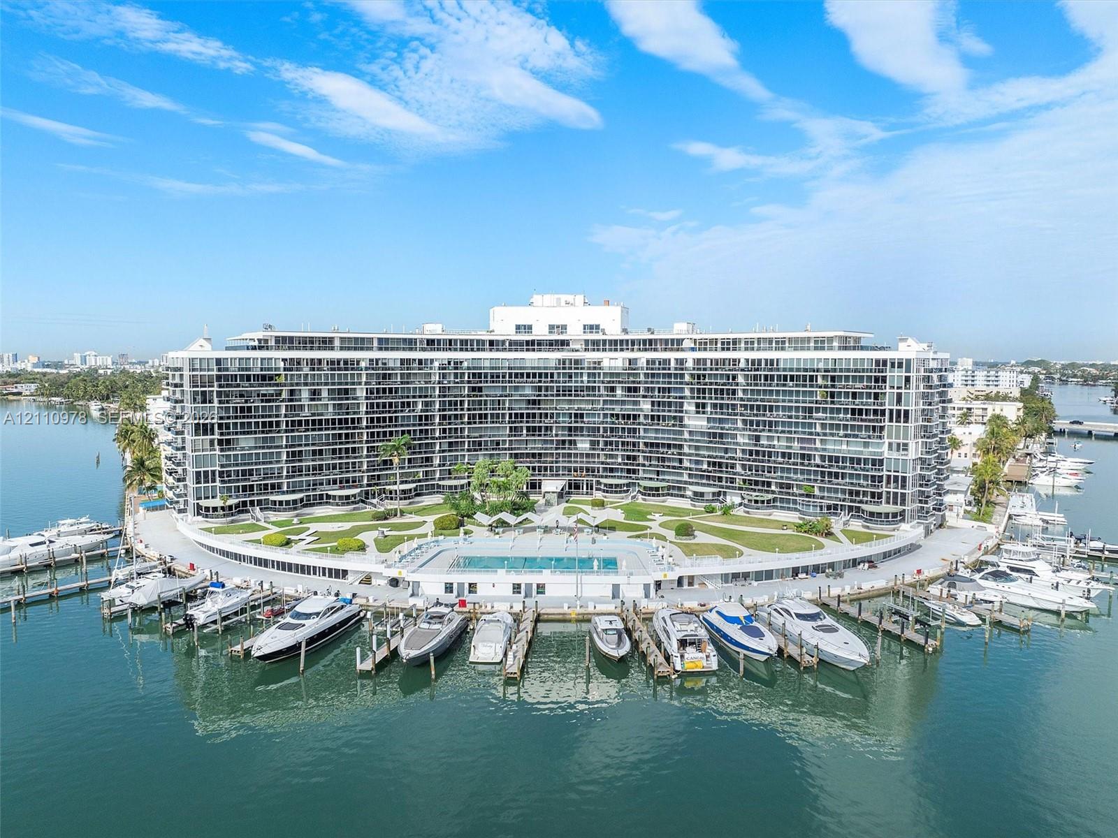 Waterfront multi-story residential building featuring private deep-water boat slips, an expansive exterior swimming pool, and manicured grounds
